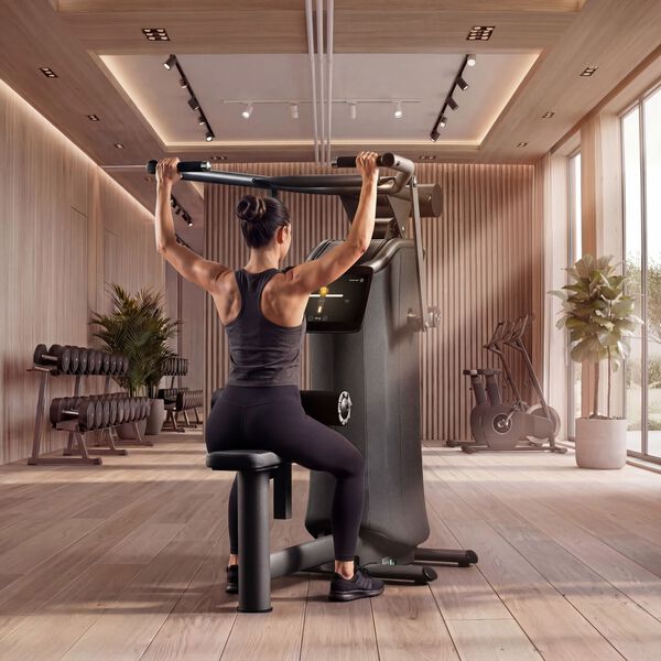 Frau trainiert ihren R&uuml;cken an einem EGYM-Latzugger&auml;t in einem modernen Fitnessstudio mit Hanteln und Cardioger&auml;ten im Hintergrund.