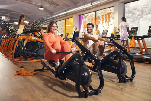 Mitglieder trainieren auf Ruderger&auml;ten in einem Basic-Fit Club, w&auml;hrend andere Cardioger&auml;te im Hintergrund nutzen.