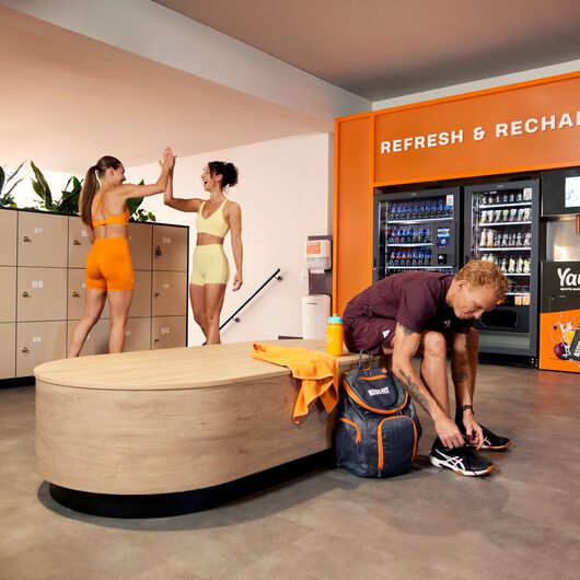 Mann, der auf einer Bank sitzt und seine Schn&uuml;rsenkel in einem Basic-Fit-Club bindet.