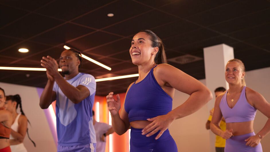 A group takes part in a bodyjam class, performing dance steps together while following the instructor in the fitness studio.