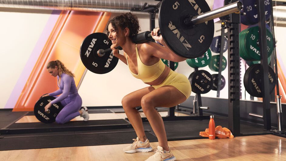 Personal trainer guiding a woman during a lunge exercise in a functional training area inside a Basic-Fit gym