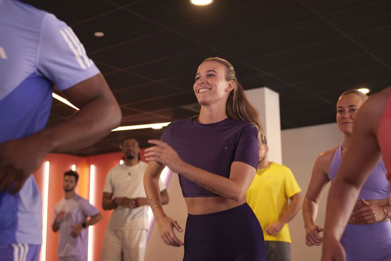 Een groep mensen voert geco&ouml;rdineerde dansbewegingen uit terwijl ze naar de voorkant van de studio gericht zijn tijdens een groepsles.