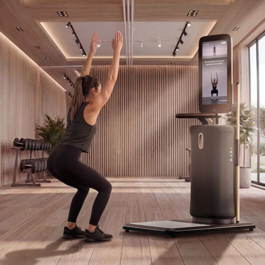 Frau folgt einer gef&uuml;hrten Anleitung f&uuml;r Kniebeugen mit dem eigenen K&ouml;rpergewicht auf einem EGYM-Bildschirm in einem modernen Fitnessstudio.