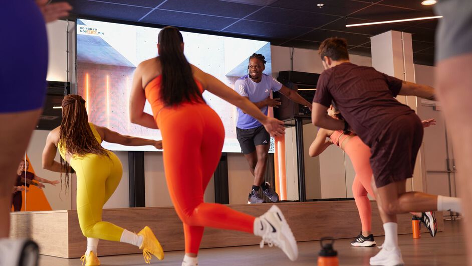 Un grupo participa en una clase de bodycombat y realiza movimientos de golpe siguiendo al instructor en el escenario.
