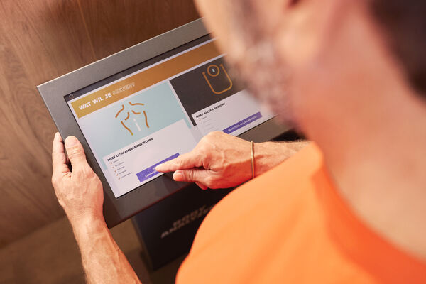 Lid gebruikt de Basic-Fit Body Analyzer om een lichaamssamenstellingsmeting te starten via het touchscreen.