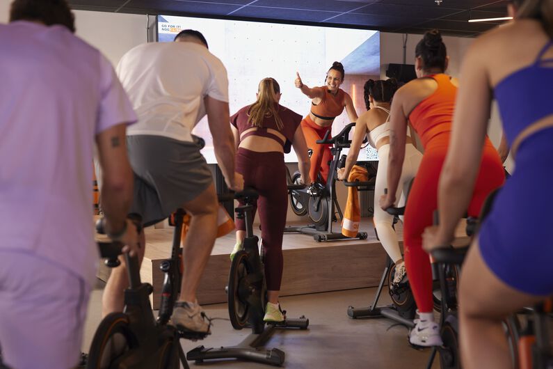 Groepscyclingles met mensen die op hometrainers fietsen in een fitnessstudio.