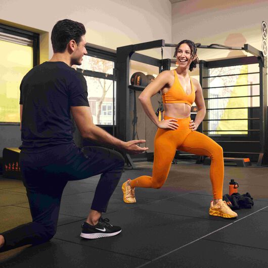 Personal Trainer, der einer Frau in einem Basic-Fit-Club eine &Uuml;bung erkl&auml;rt.