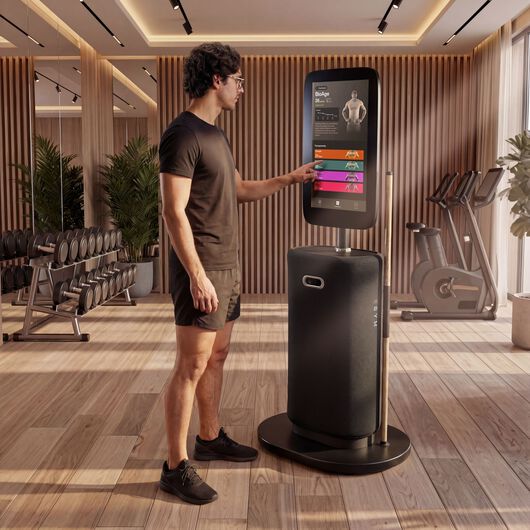 Mann steht an einer EGYM-Onboarding-Station und w&auml;hlt Optionen auf dem Touchscreen in einem Fitnessstudio aus.