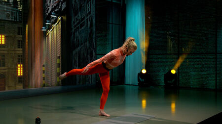 Woman balancing on one leg during a video workout in a studio, focused and controlled.	
