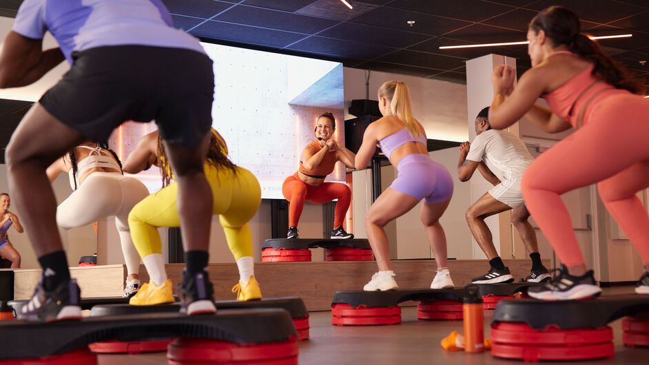 Los participantes realizan una clase de steps con sentadillas y movimientos sobre plataformas.