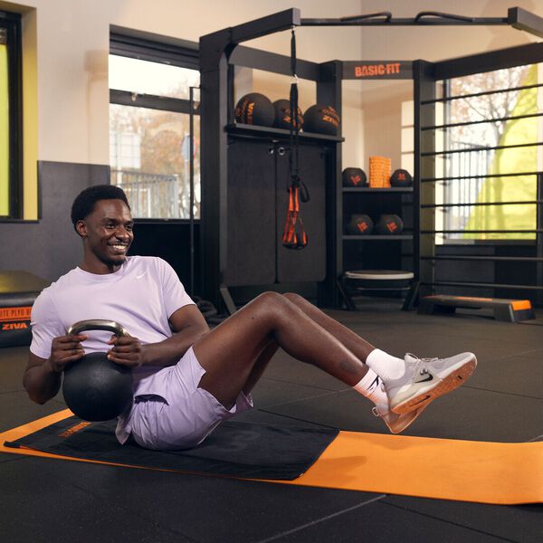 Homme r&eacute;alisant des rotations russes avec un kettlebell sur un tapis.