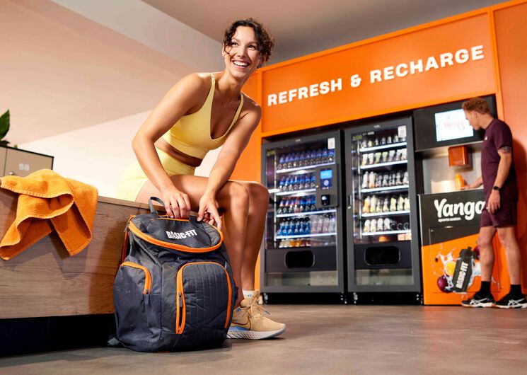 Frau, die auf einer Bank sitzt und ihre Basic-Fit-Sporttasche packt.