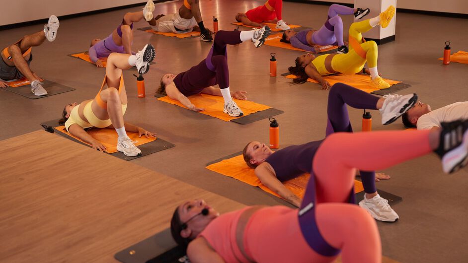 deelnemers staan met weerstandsbanden rond hun benen en voeren onderlichaambewegingen uit in een fitnessstudio