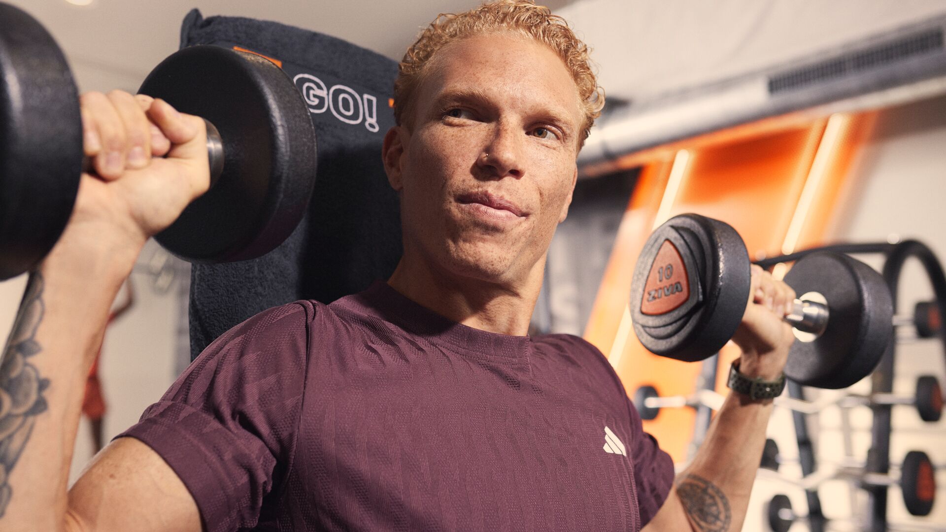 Hombre hace un press de hombros con mancuernas en el gimnasio