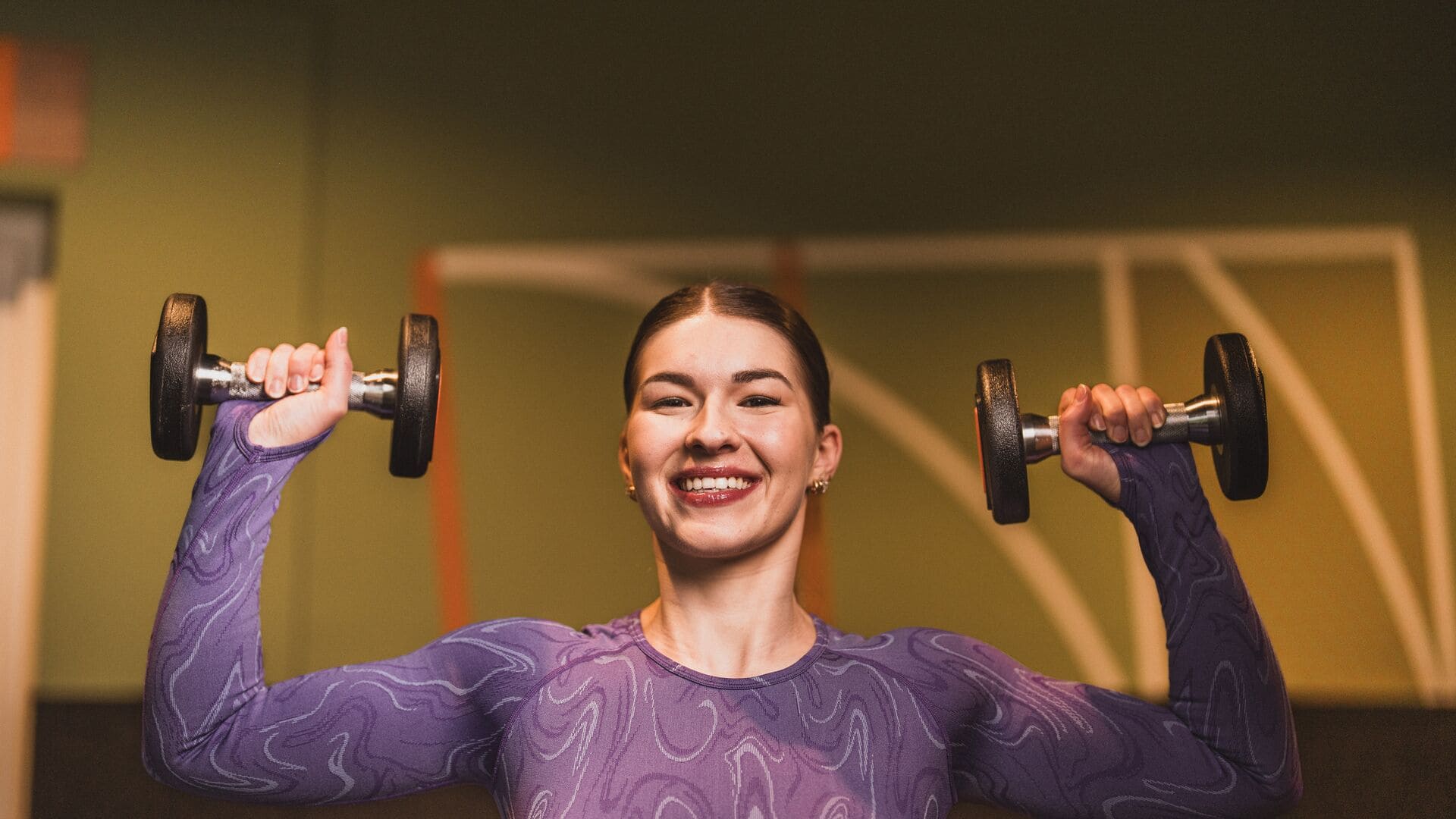 Lachende Frau hebt Hanteln während ihres Trainings in einem Basic-Fit-Studio.