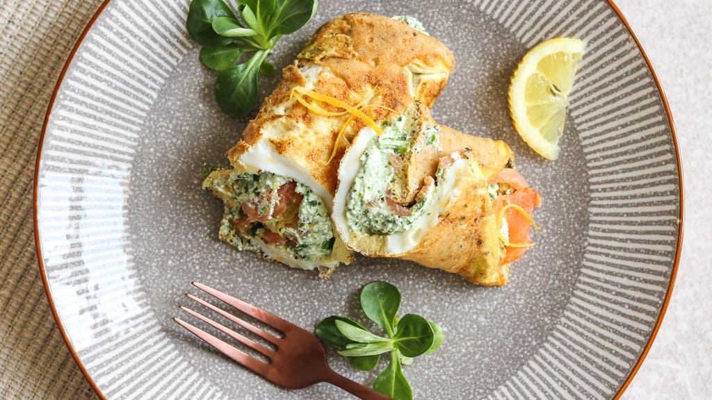 Teller mit frischen Omelett-Wraps, gefüllt mit Lachs und Spinat, serviert mit Zitrone und Gemüse.