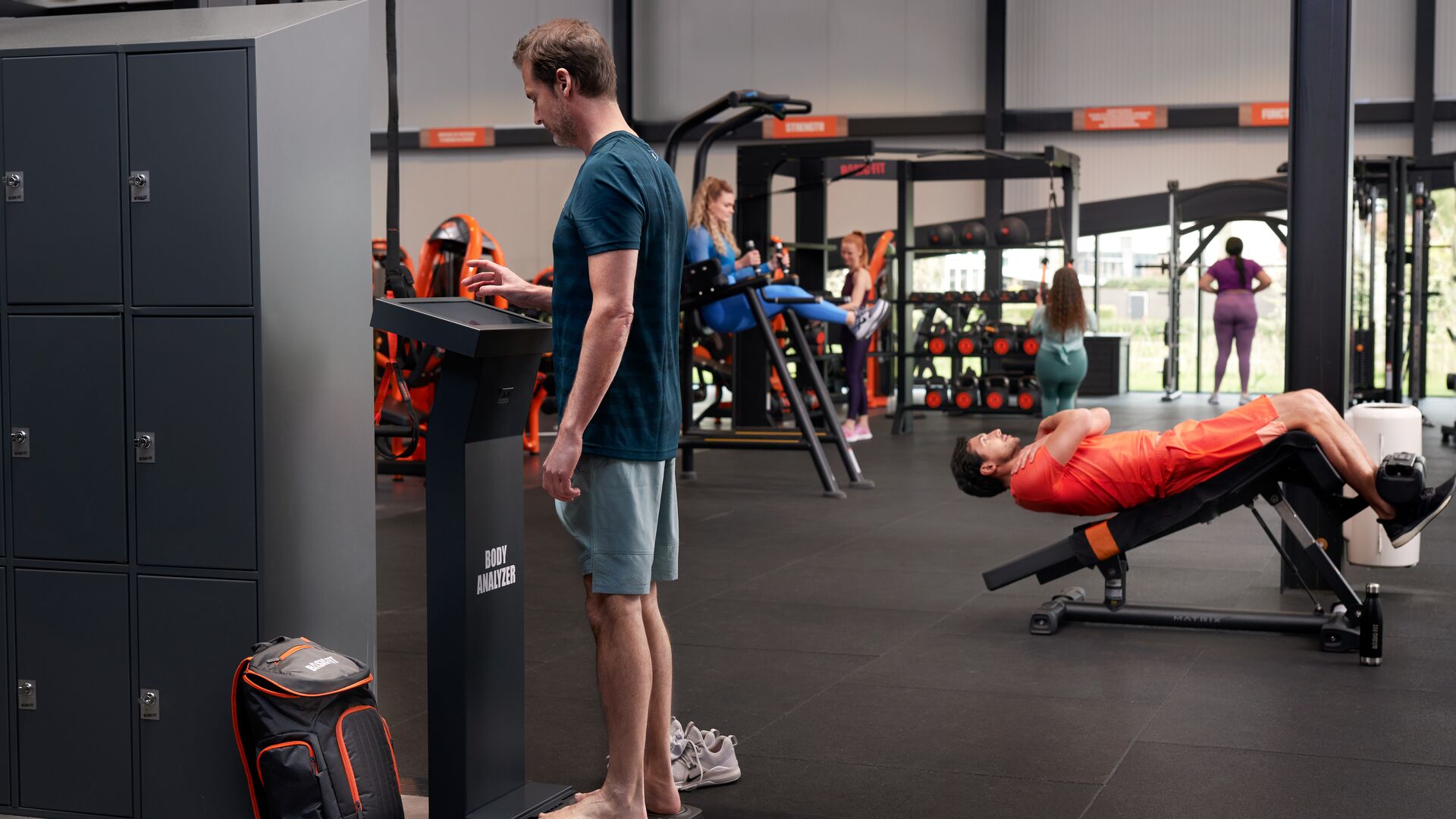 Man using the Body Analyzer kiosk in a Basic-Fit club while others train in the background
