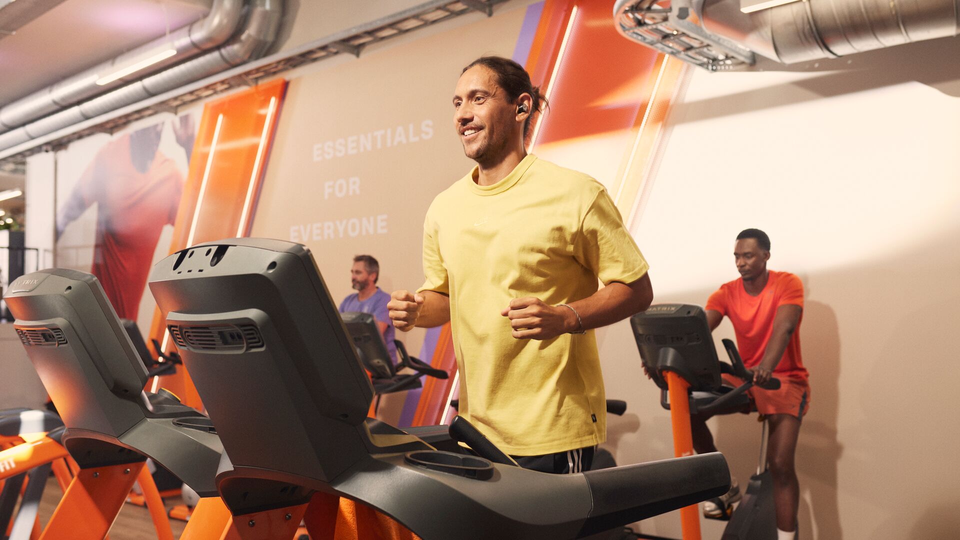 Man running on a treadmill in a Basic-Fit cardio area with other members training in the background.