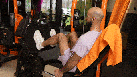 A person uses the leg press machine in a Basic-Fit gym, pushing the platform away and bending the knees to return to the start position.