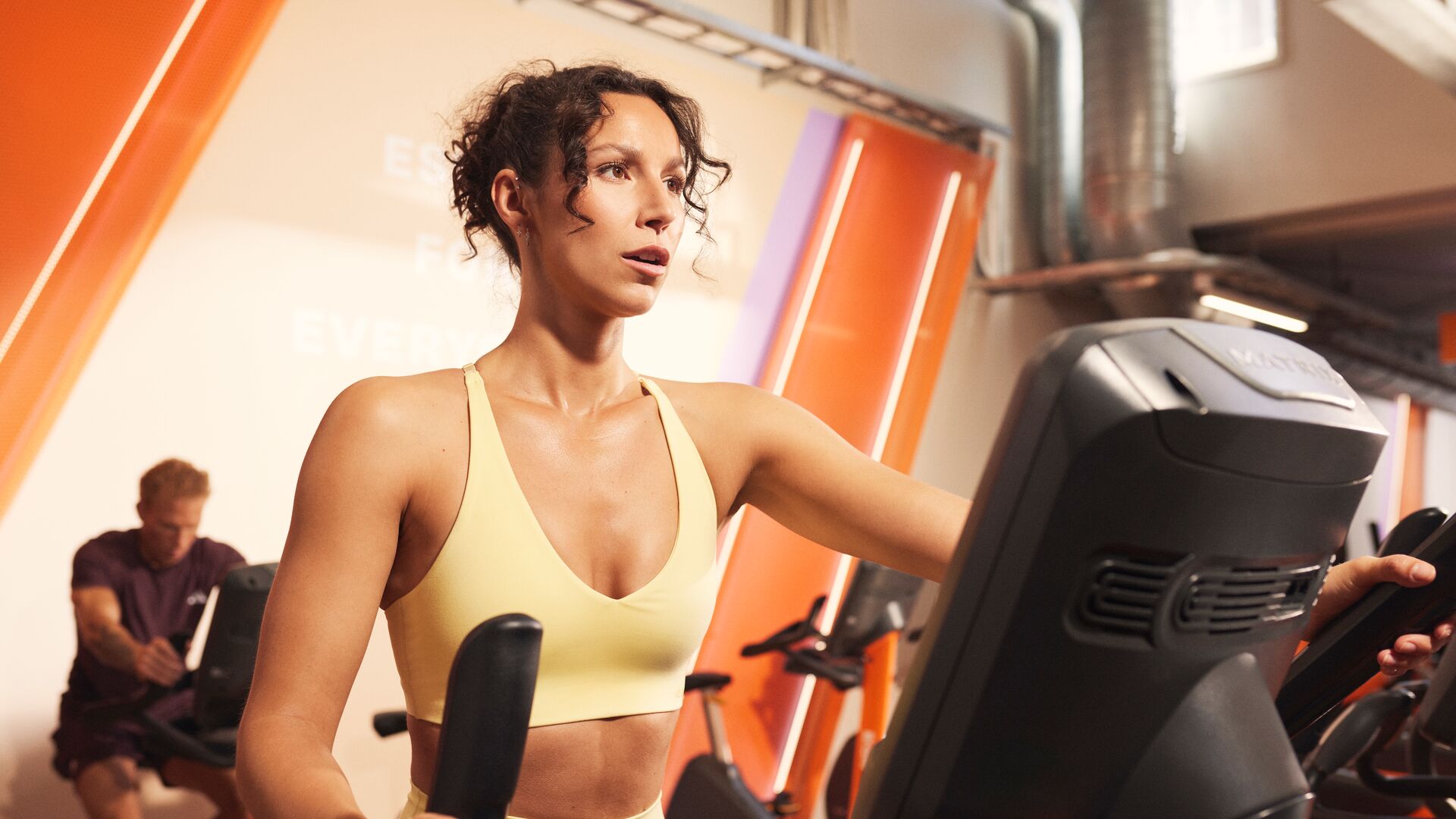 Woman training on a cross trainer in a Basic-Fit cardio area.