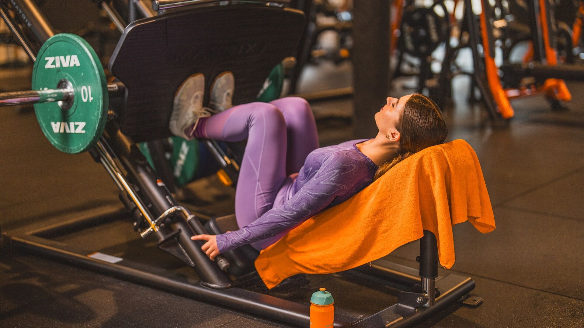 A woman in a purple outfit trains on the leg press machine at Basic-Fit, focused and steady.
