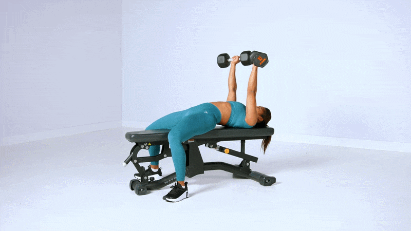 Mujer hace un press de pecho con mancuernas en un banco en un entrenamiento de estudio