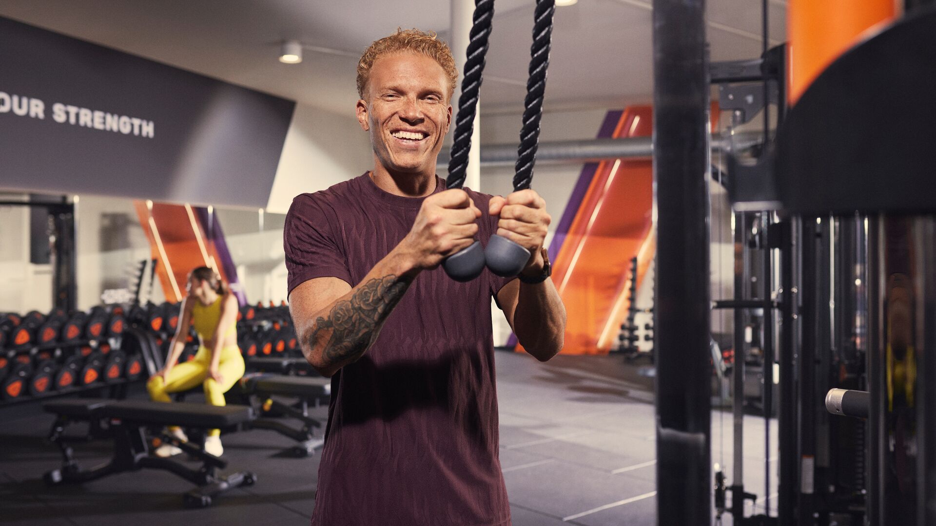 Man smiling while using rope handles in a Basic-Fit strength training area.