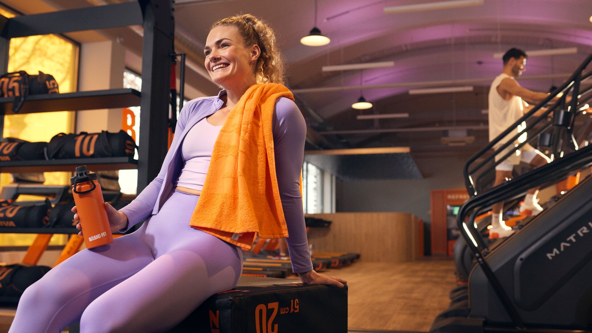 Femme se reposant après son entraînement à la salle de sport pendant qu’un homme s’entraîne sur un stair climber