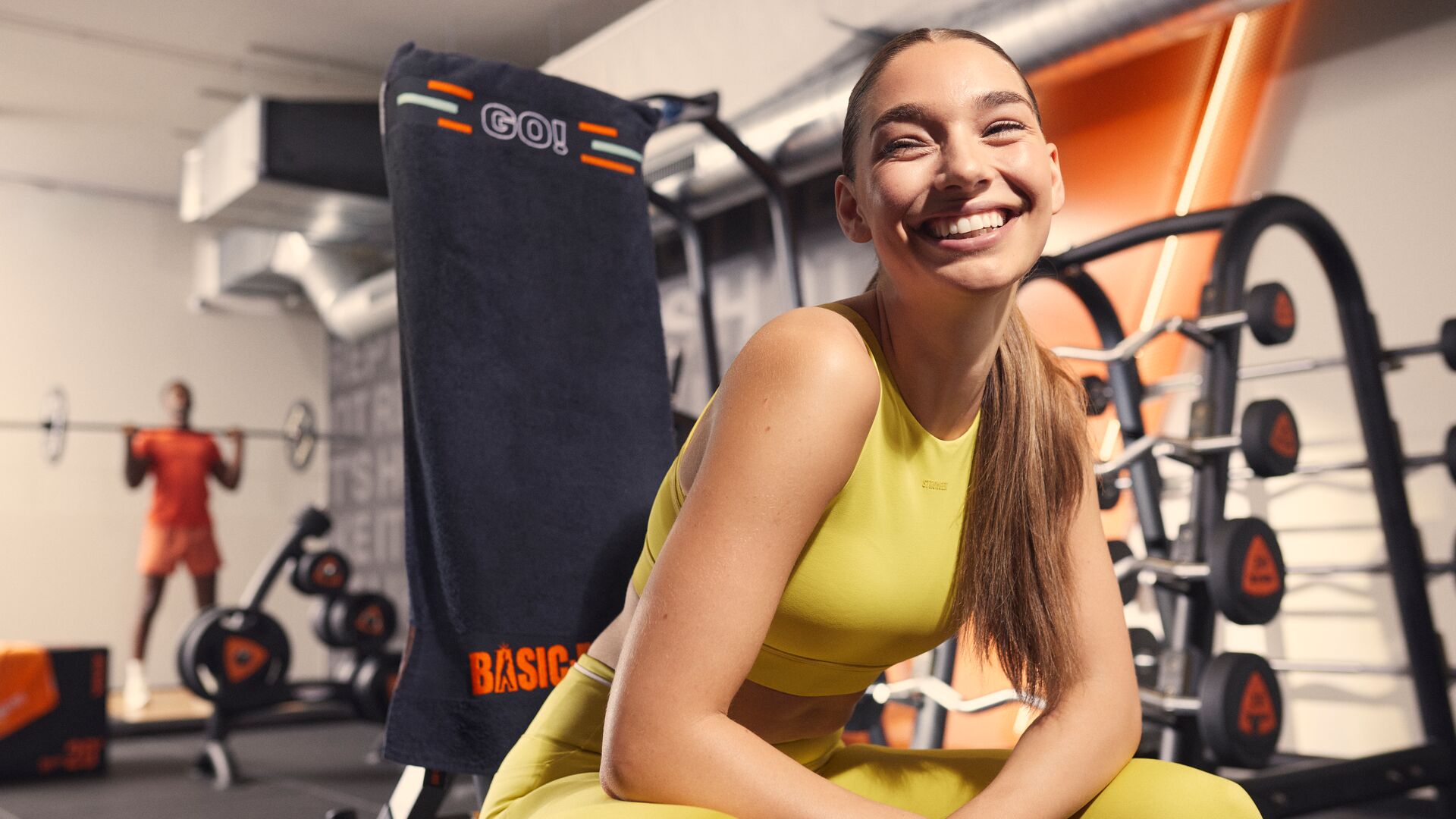 Mujer sonríe mientras descansa en una máquina de fuerza en el gimnasio