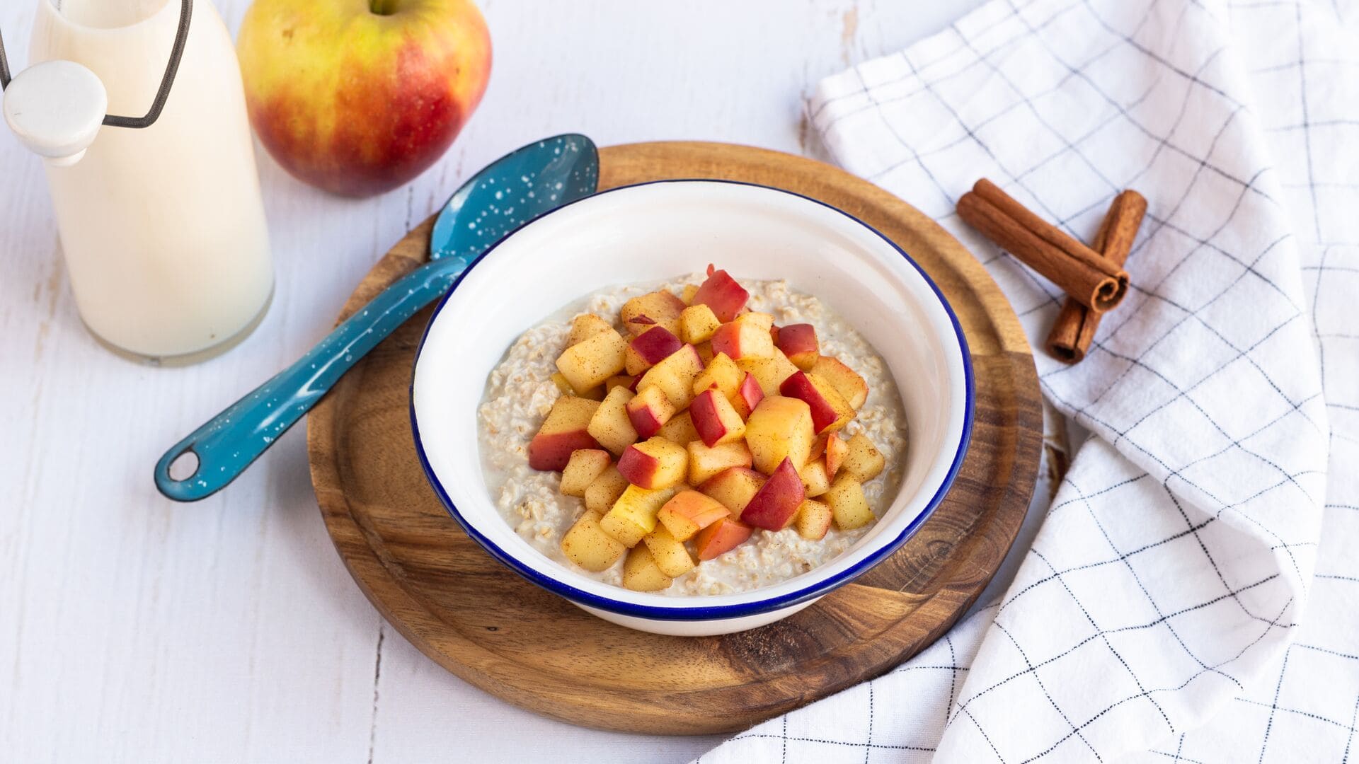 Schüssel mit Overnight Oats, belegt mit warmen Apfelstücken und Zimt, serviert auf einem Holzbrett.